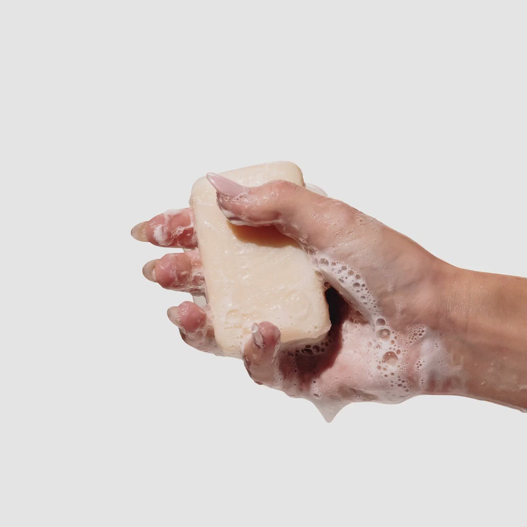 Video of hand holding and rubbing the unwrapped beekman 1802 Vanilla Woods Palm-Sized Goat Milk Soap which is wet and covered in suds.