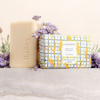 Beekman 1802 wrapped lavender goat milk soap and unwrapped lavender goat milk soap next to each other surrounded by lavender.