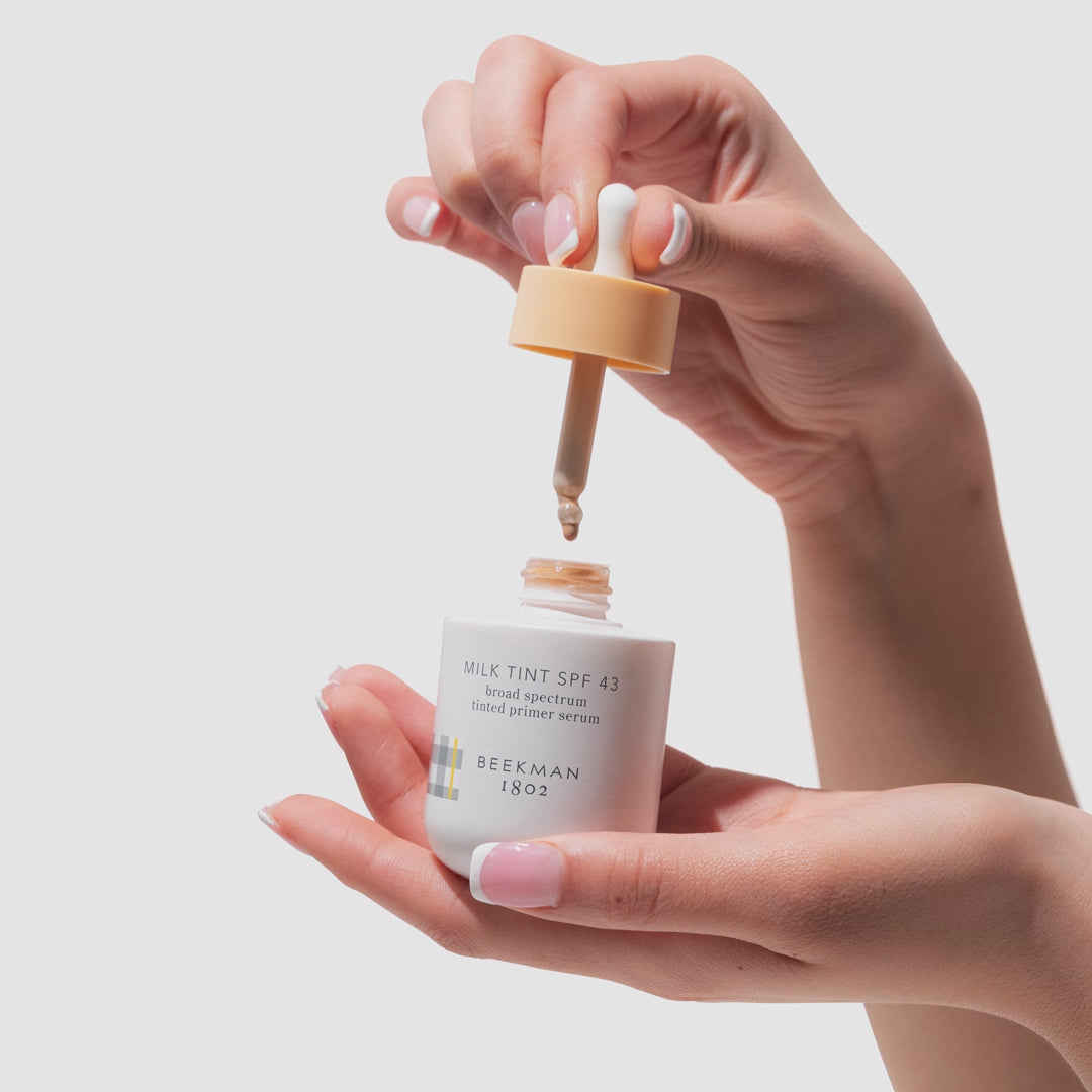 GIF of hand holding Beekman 1802 Milk Tint SPF 43 Tinted Primer Serum while other hand is squeezing product out of dropper.