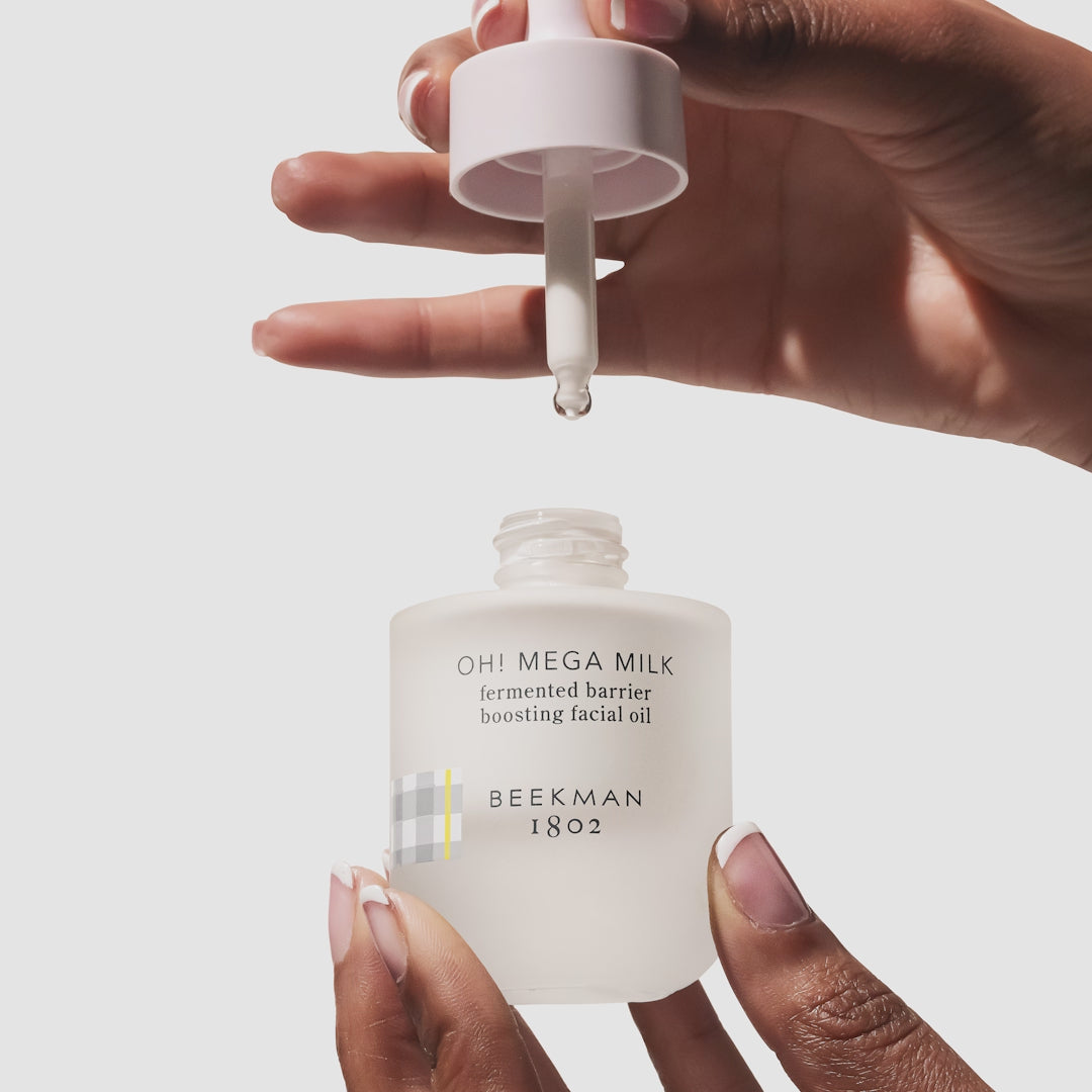 A video shot of a hand holding a bottle of Beekman 1802's Oh! Mega Milk Fermented Facial Oil and squeezing the dropper to show the texture of the facial oil.