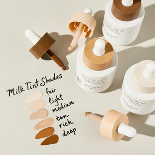 image of Beekman 1802 Milk Tint SPF 43 Tinted Primer Serum bottles next to writing that says "milk tint shades" with shade names next to texture swatch.