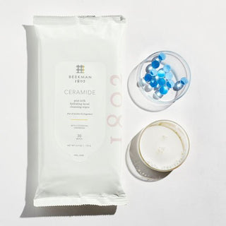beekman 1802 ceramide face wipes next to a glass of goat milk and a petri dish with blue gel beads.